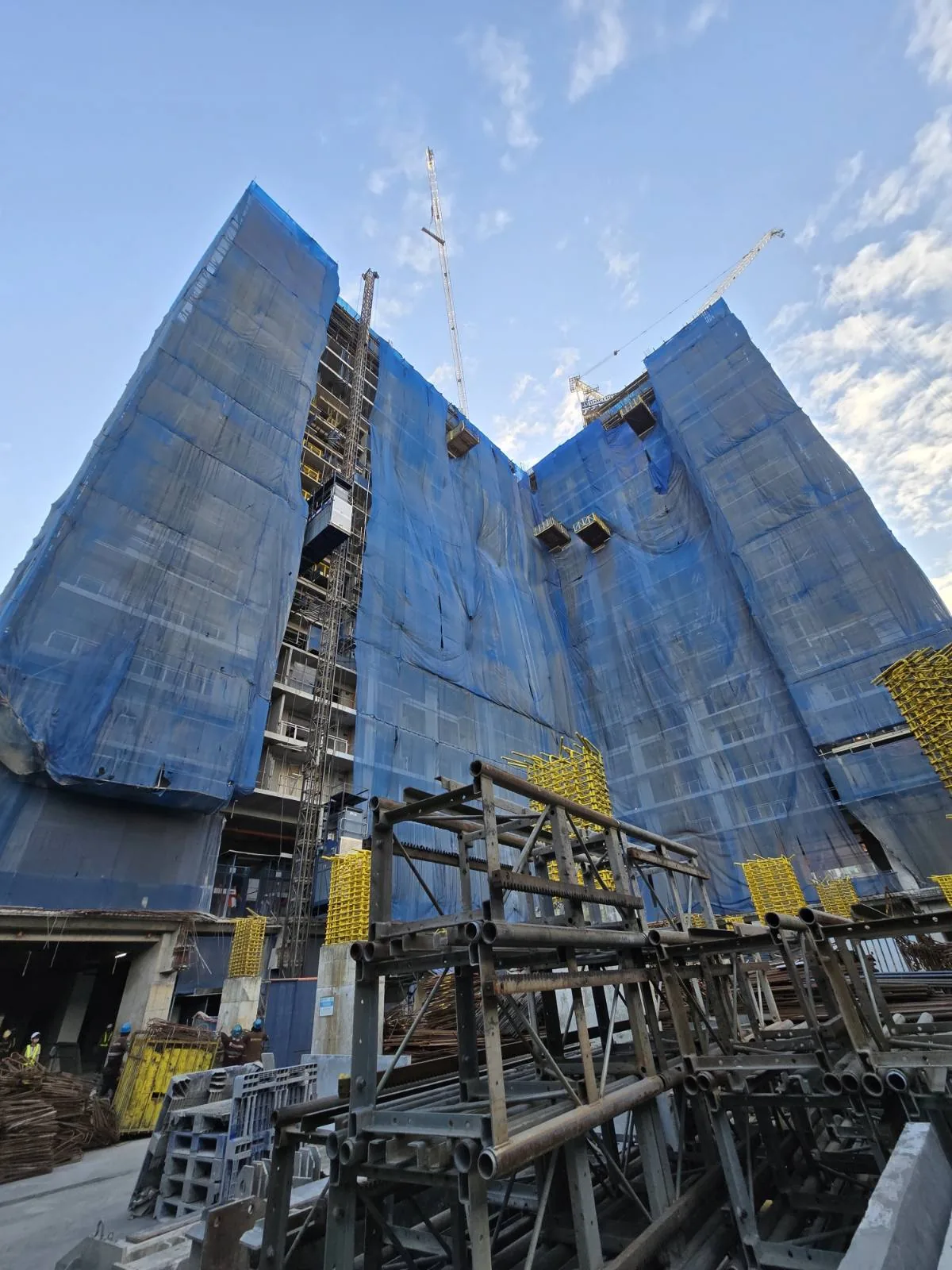 Sage Residences tower facade under construction, wrapped in scaffold netting
